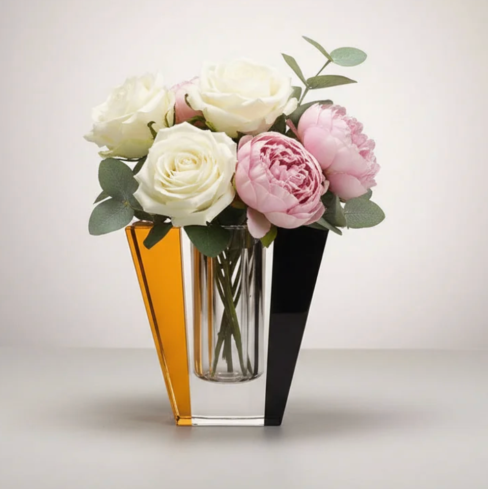 The Solar Prism Crystal Diffuser in Sapphire & Amber by Frave Home stands out on a light surface with its modern design, showcasing amber and black sections accented by white roses, pink peonies, and green foliage against a neutral backdrop.