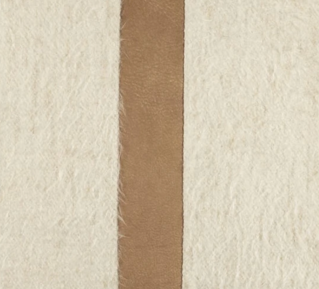 The Bruno Pillow - Bisque & Camel from Moss Studio features a vertical camel leather contrast band running down the center of its textured, off-white, hairy surface, elegantly dividing it into two sections and adding a touch of luxury perfect for modern interiors.
