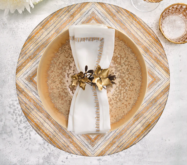 A gold and black Kim Seybert Magnolia Napkin Ring Set of 4, shaped like a burnished gold magnolia flower, secures a white napkin resting in a decorative bowl.