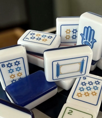 A scattered collection of acrylic Mahjong tiles from the Mahjong Tile Set - Brilliant Nights Hanukkah in Gift Box, featuring blue and gold designs, including Stars of David, a hamsa, and a scroll.