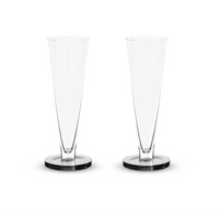 Two empty, clear Tom Dixon Puck Flute Glasses (Set of 2) are standing side by side on a plain white background.