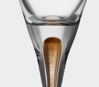 A close-up of the Orrefors Kosta Boda Intermezzo Champagne Glass Gold Set of 2, featuring mouth-blown glass with a tapered base and a drop-shaped gold element embedded inside—an elegant design inspired by Erika Lagerbielke.