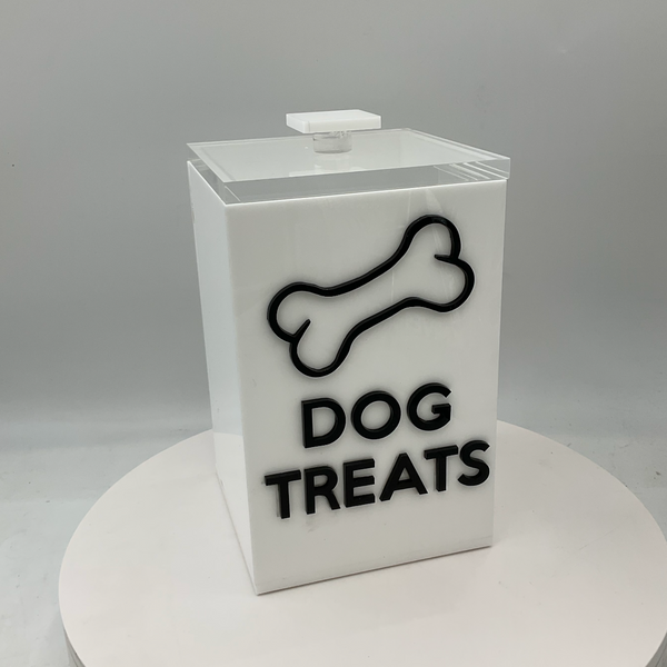 The Eye Candy Dog Treats Canister is a white rectangular holder with a clear lid, labeled "DOG TREATS" in bold black letters and decorated with a black dog bone outline.