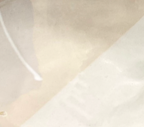 A close-up of translucent, slightly crumpled paper rests on Urban Dinnerware – Custom plates by Alex Marshall Studios, with a faint diagonal seam and white string in the upper left. The softly textured background is light.