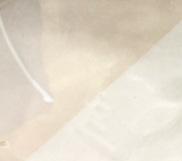 A close-up of translucent, slightly crumpled paper rests on Urban Dinnerware – Custom plates by Alex Marshall Studios, with a faint diagonal seam and white string in the upper left. The softly textured background is light.