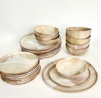 The Urban Dinnerware - Custom set by Alex Marshall Studios features handmade beige and cream ceramic plates and bowls with an organic design, arranged in neat stacks. Microwave and dishwasher safe.