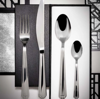 The Degrenne Normandy Flatware 5 Piece Set, featuring stylish Art Deco silverware, is displayed on a black and white geometric-patterned background.