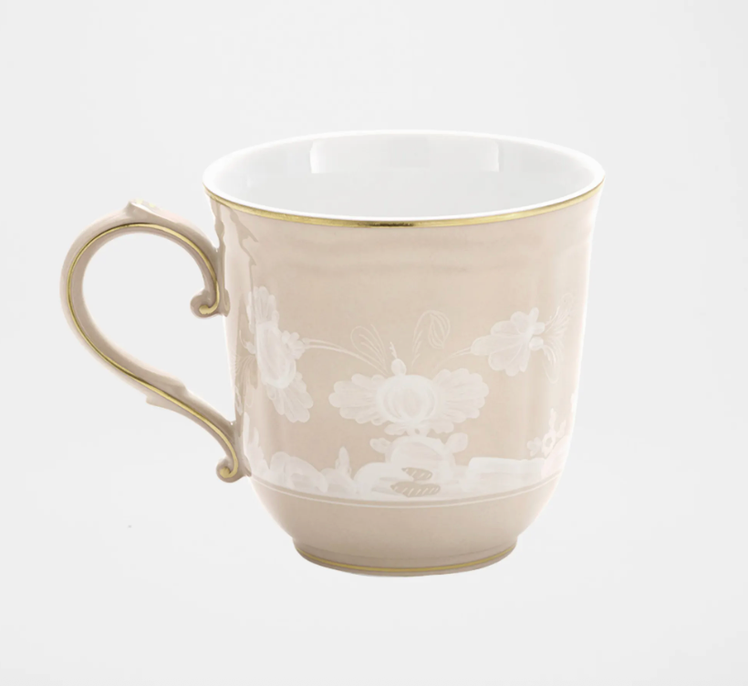 The Oriente Italiano Beige Meringa mug by Ginori 1735 is a beige ceramic piece with a gold rim and handle, adorned with a delicate white floral pattern, inspired by timeless elegance, shown against a plain white background.