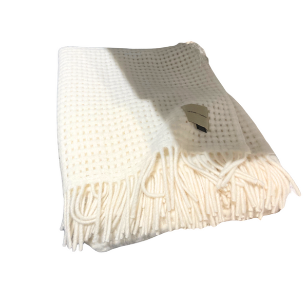 The Thread & Butter Waffle Alpaca Throw - Ivory is a cream-colored, sustainable alpaca blanket with a waffle texture, fringed ends, and a small tag, shown folded on a white background.