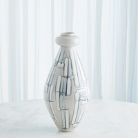 The Spindel Vase Grey Blue by Global Views/Surya, a tall white Portuguese ceramic piece with blue and gray linear patterns, stands on a round white surface before sheer vertical white curtains.