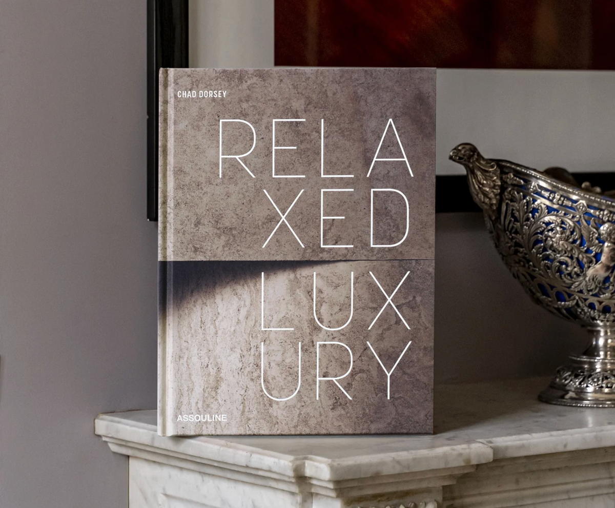 Relaxed Luxury by Assouline, authored by interior designer Chad Dorsey, stands on a marble mantel next to a silver bowl. The cover displays bold white text against a textured stone backdrop.