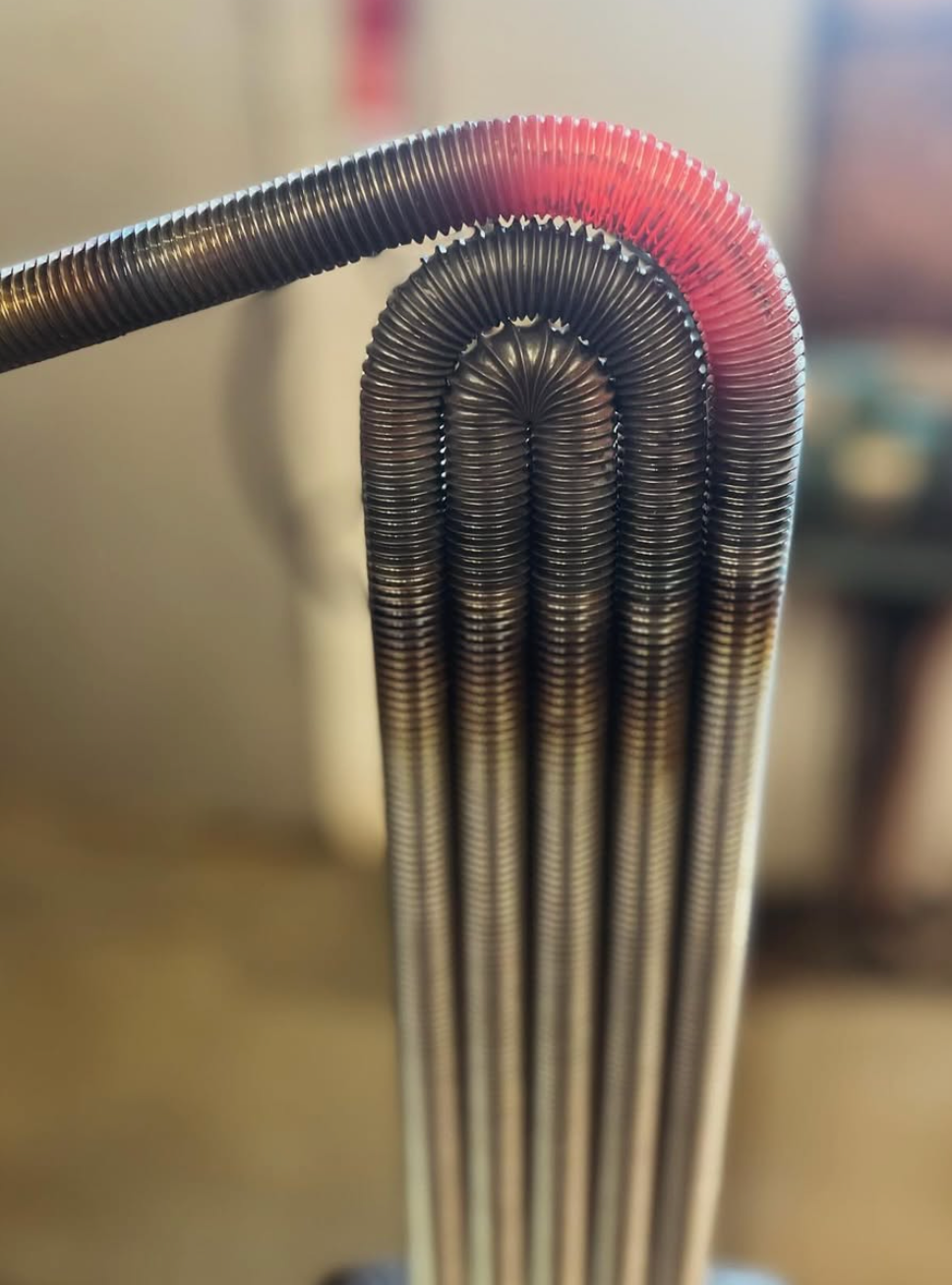 Close-up of the Heater Vase - Black Splash by Matt Kolbrener: several tightly coiled metal tubes bend into glowing U-shapes, creating a striking, industrial-modern accent ideal for contemporary decor or pairing with artisan glass art.
