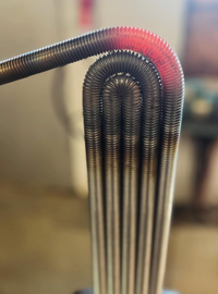 Close-up of the Heater Vase - Black Splash by Matt Kolbrener: several tightly coiled metal tubes bend into glowing U-shapes, creating a striking, industrial-modern accent ideal for contemporary decor or pairing with artisan glass art.