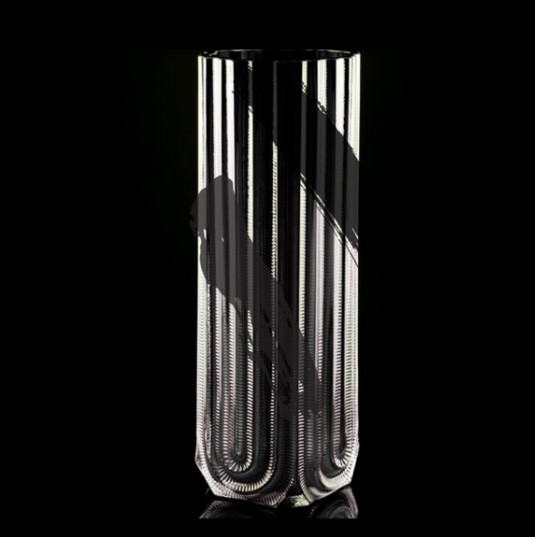 The Heater Vase - Black Splash by Matt Kolbrener is a tall, handblown glass vase with vertical grooves and a unique U-shaped base. Set against a black background, reflections highlight its artisan design and craftsmanship.