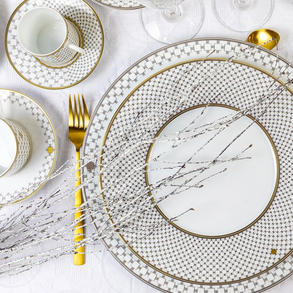 An elegant table is set with Robert Haviland & C. Parlon’s Home Platinum Dinnerware, gold utensils, and clear wine glasses. Silver branches arranged on plates atop a white tablecloth add a luxurious touch.