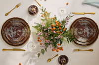 Elegant table set with Ginori 1735's Oriente Italiano Castagna china, brown and white details, gold cutlery, clear glassware, and a centerpiece of orange berries and pink flowers atop a crisp white cloth. Made in Italy.