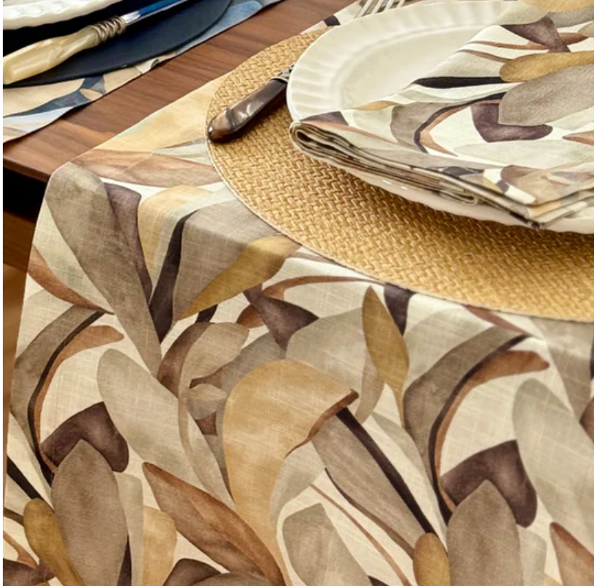 Close-up of a dining table featuring Bodrum’s Flora Napkin Set of 4, paired with a beige and brown leaf-patterned table runner, white plate, knife, and woven placemat for an inviting fall-inspired look.