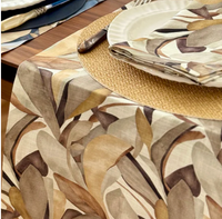 Close-up of a dining table featuring Bodrum’s Flora Napkin Set of 4, paired with a beige and brown leaf-patterned table runner, white plate, knife, and woven placemat for an inviting fall-inspired look.