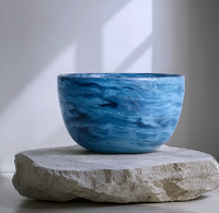 The Nashi Home Swirl Colored Resin Deep Bowl, featuring marbled swirls, rests on a rough rectangular stone slab in natural light against a plain white wall.