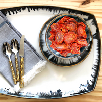 The Michael Wainwright Fjord Oval Platter – Large holds a bowl of sun-dried tomatoes, paired with a gray napkin and gold-handled cutlery on wood—a sophisticated addition to your kitchenware collection.