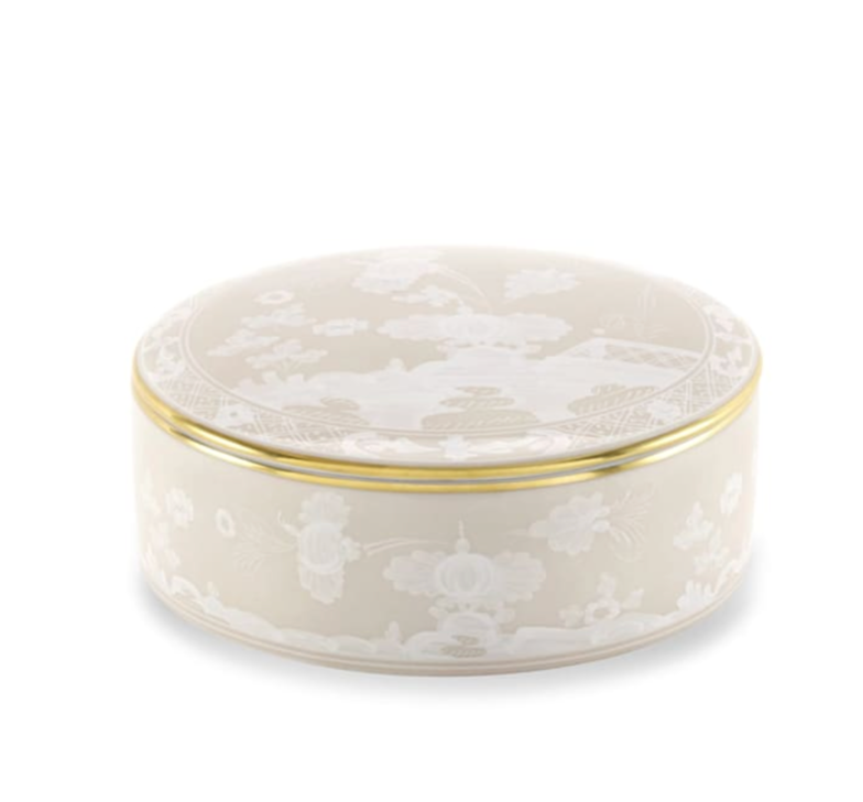 The Ginori 1735 Oriente Italiano Meringa Round Box with Lid is a beige ceramic trinket box, adorned with white floral patterns and finished with a slim gold rim near the top.
