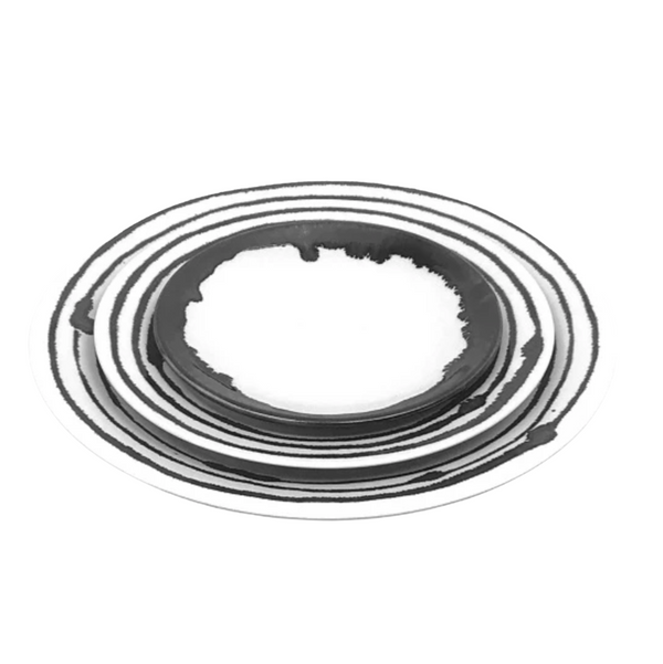The Michael Wainwright Linea Dinnerware set includes three black and white ceramic plates, each with a hand-painted concentric circle pattern, stacked elegantly together.