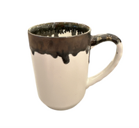 The Linea Dinnerware ceramic mug by Michael Wainwright features a white base with a dark brown, uneven glaze dripping from the rim onto the handle, set against a white background.