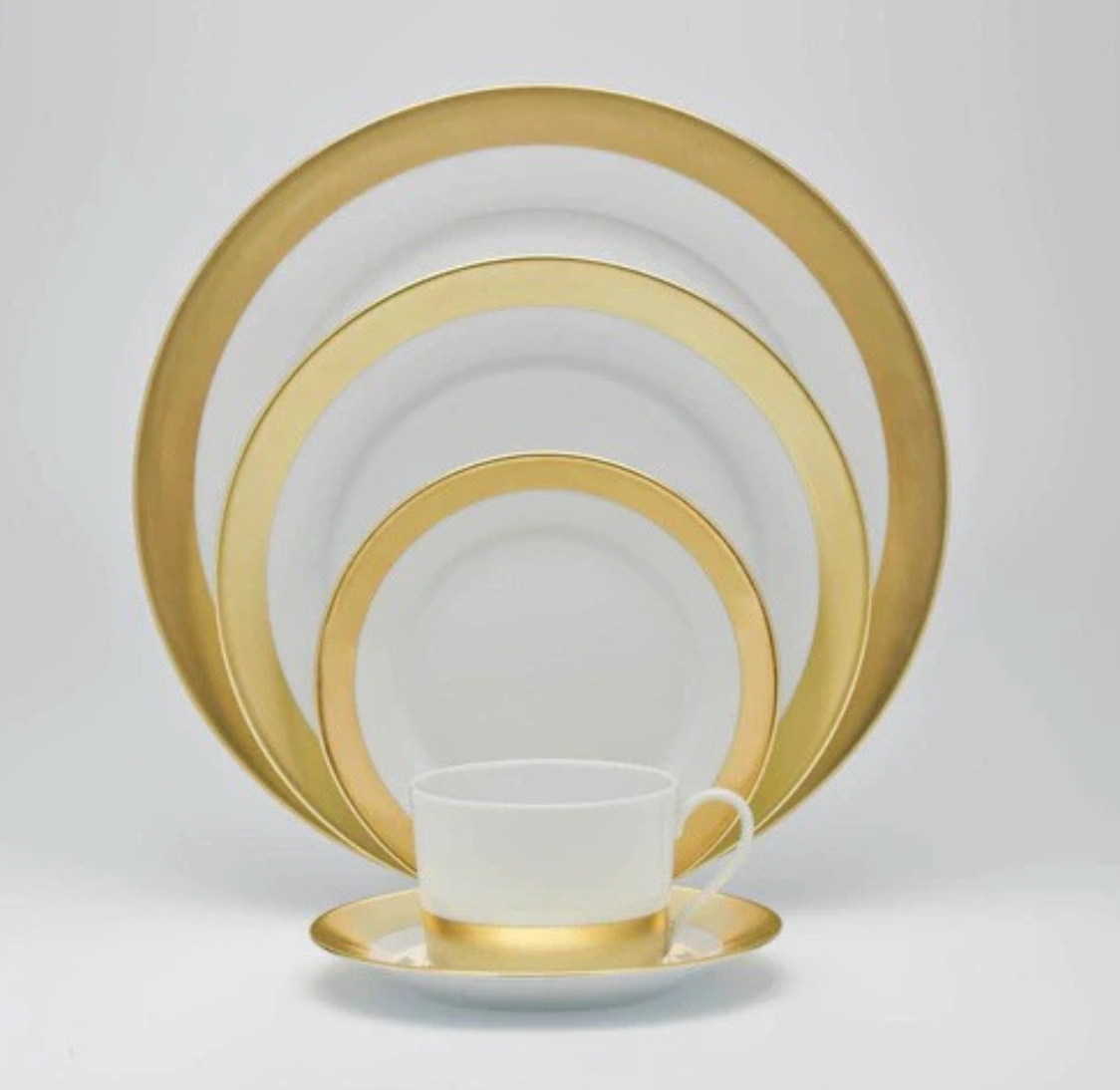 The Danielle Gold Dinnerware set by Royal Limoges features a cup and saucer, small plate, medium plate, and two large plates with gold rims, all arranged by size against a plain white background.