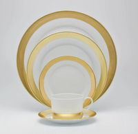 The Danielle Gold Dinnerware set by Royal Limoges features a cup and saucer, small plate, medium plate, and two large plates with gold rims, all arranged by size against a plain white background.