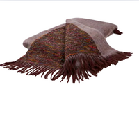 The Coco Throw by Mantas Ezcaray is a folded, fringed double-sided blanket featuring a multicolored woven center, solid maroon edges, and Chanel-inspired style, displayed on a white background.