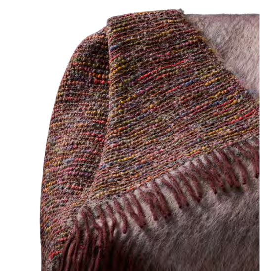 A close-up of the Coco Throw by Mantas Ezcaray, a double-sided blanket with multicolored threads and fringed edges reminiscent of Chanel fabric, draped over a light grey fuzzy surface.