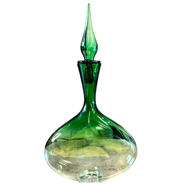 The Emerald Oval Bottle with Top by Andy Koupal features hand-blown green glass with a wide base, narrow neck, pointed stopper, and glossy translucent finish—exemplifying fine artisan craftsmanship.