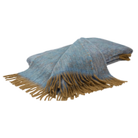 The Diana Mohair Throw by Mantas Ezcaray is a folded, soft blue-gray blanket with thick brown fringe, elegantly displayed on a white background.
