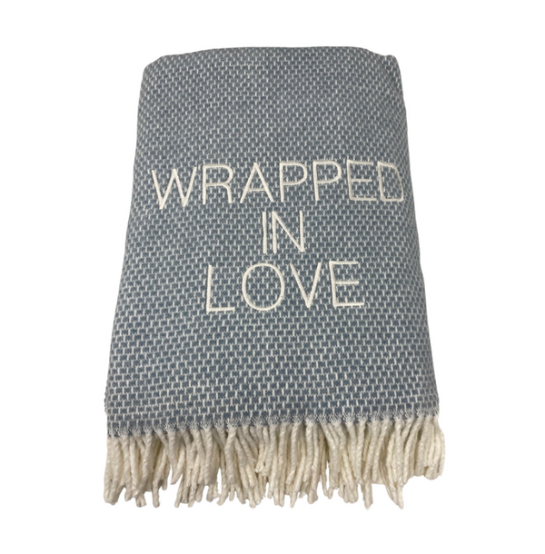 The Wrapped in Love Throw by A Soft Idea is a gray woven blanket with white fringe and "WRAPPED IN LOVE" embroidered on the front. Super soft and machine washable, it makes a thoughtful holiday gift for any cozy home.