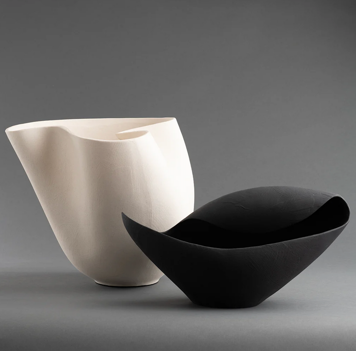 The Bernard Bowl - Black by FlowDecor Inc. is a sculptural ceramic vessel with an asymmetrical, rounded form, shown on a gray surface against a gray background for a modern decorative touch.