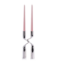 The Zodax Interlock Candle Holder in polished nickel features a modern twisted design with a split base, securely holding two tall pink taper candles—an ideal accent for contemporary décor.