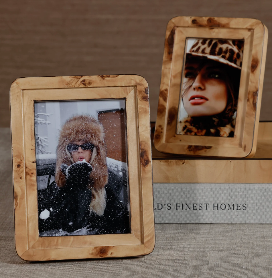 Two Zodax Valari Burl Veneer Frames display portraits of women in winter hats—one upright with a woman in a leopard-print hat, the other leaning against it showing a woman in a fur hat with falling snow.