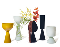 Five modern Fiorelli Vases Ash from Current Home NY—sculptural in yellow, white, and black—showcase yellow and orange flowers with green foliage, creating a striking floral arrangement against a white background.