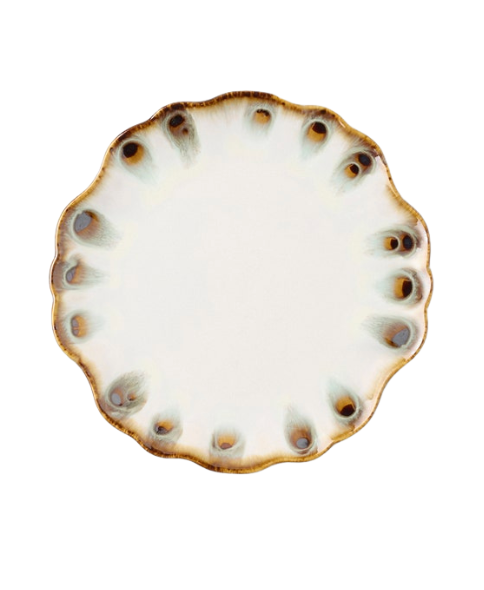 The Amoria Dinnerware by Blue Pheasant features a round ceramic plate with a scalloped, wavy edge and a crisp white center. Its rim is adorned with brown and blue-green spots created by a reactive glaze, lending the piece a rustic, hand-crafted look. This vintage-inspired serveware captures elegant charm and makes an eye-catching addition to any table setting. Shown against a plain white background.