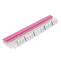 A transparent rack displays a row of pink-backed tiles from the Oh My Mahjong Amara Mahjong Tiles Set, with several acrylic pieces revealing beautiful floral and character designs.