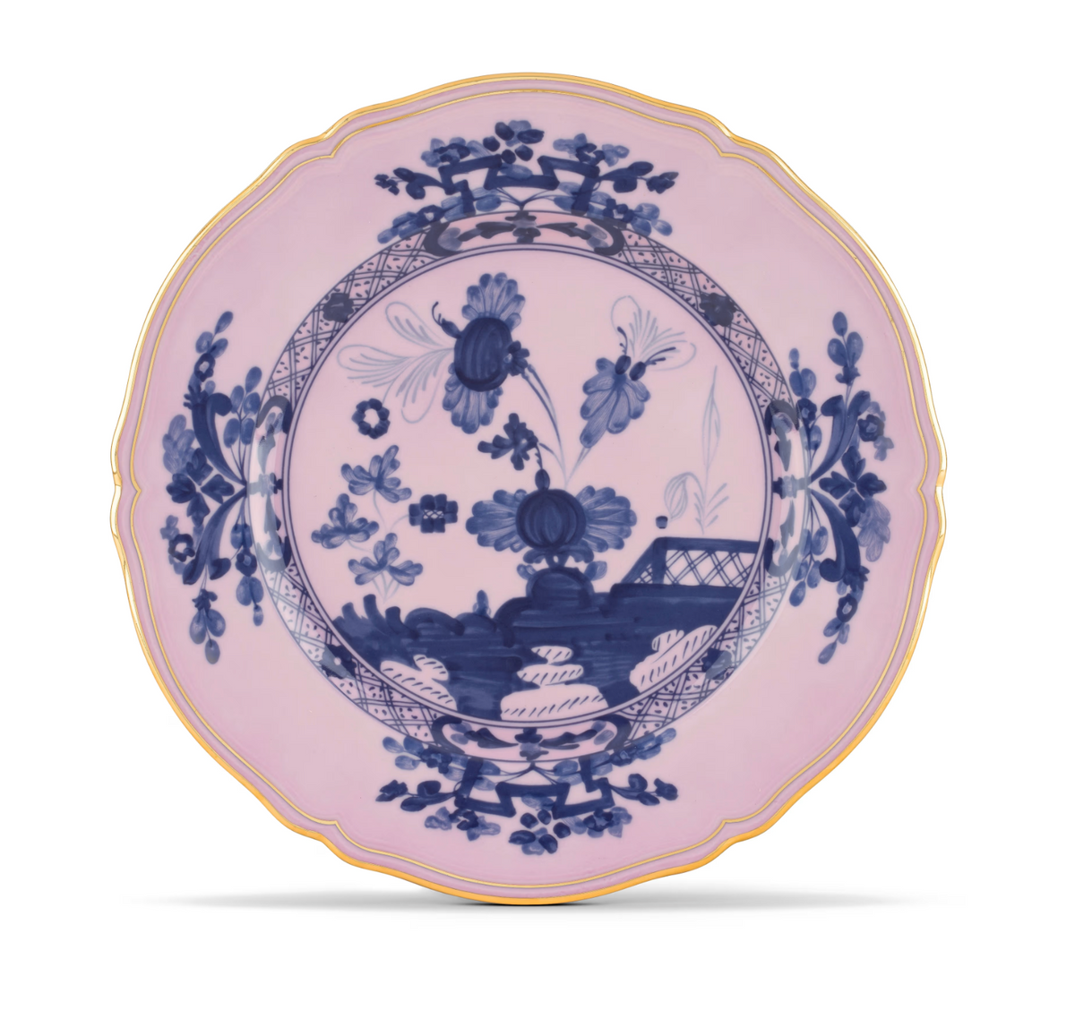 Here’s the rewritten sentence using your product data: The Ginori 1735 Oriente Italiano Dinnerware Azalea is a porcelain plate with a scalloped gold rim, showcasing a blue chinoiserie floral motif and landscape pattern on a pale pink background, inspired by timeless elegance.