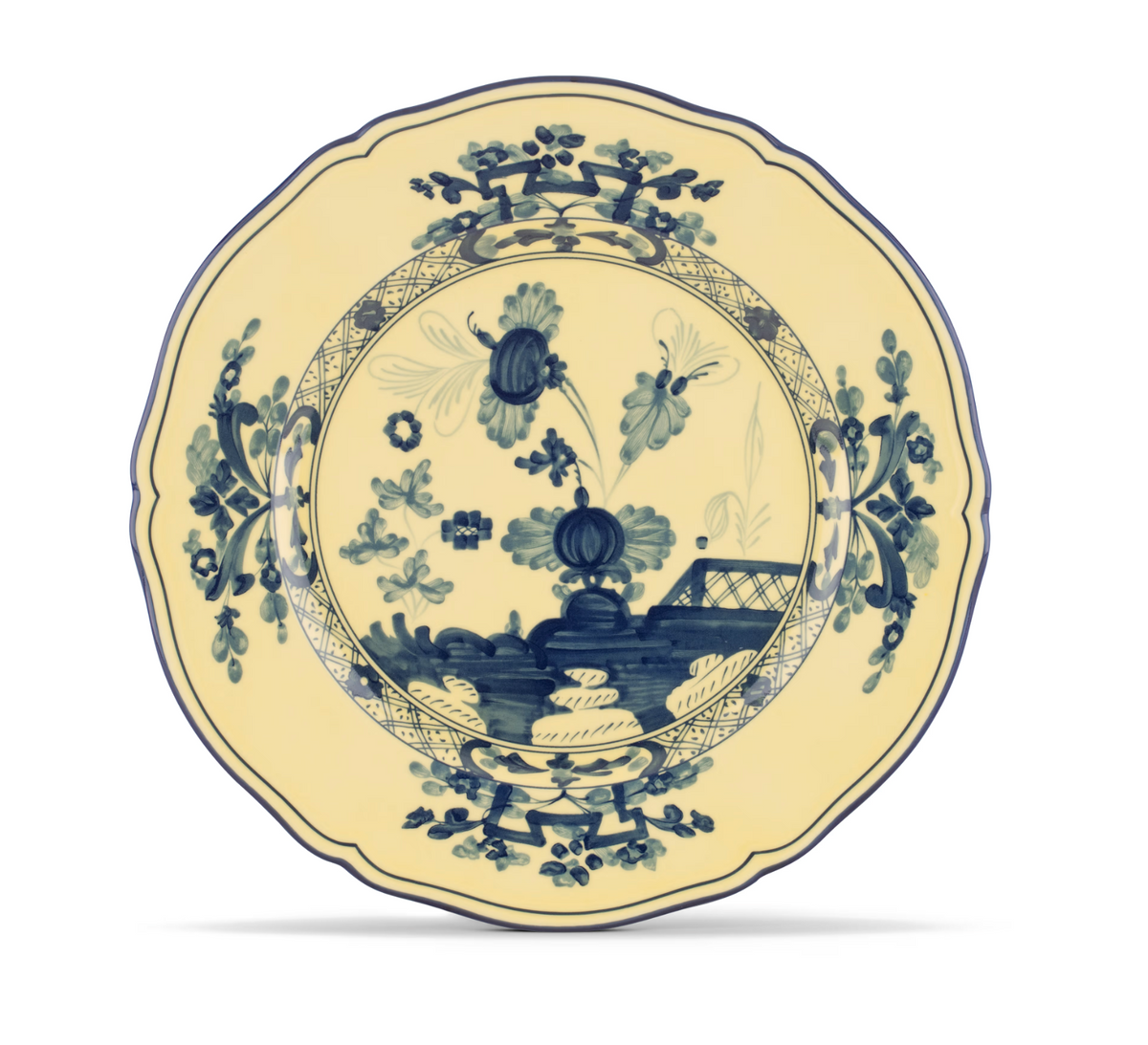 The Oriente Italiano Dinnerware Citrino plate by Ginori 1735 features a scalloped edge and is adorned with intricate blue chinoiserie-inspired floral and foliage patterns on a cream background. Reminiscent of classic Italian porcelain, it showcases a central floral motif and decorative border details.