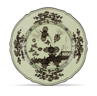 A decorative ceramic plate from Ginori 1735, the Oriente Italiano Dinnerware Bario, with scalloped edges and a black floral and nature-inspired motif on a pale green background, inspired by chinoiserie style.