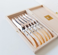 A wooden box containing the Berlingot Steak Knives Set of 6 by Claude Dozorme, each pearl-handled knife showcasing a gleaming blade, expert craftsmanship, and distinctive rivets on the handle, all neatly organized inside.