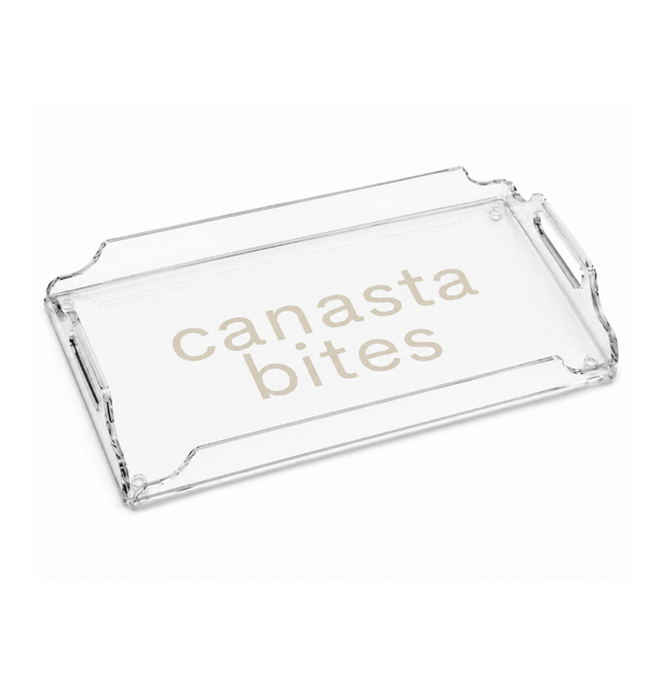 The Eye Candy Deluxe Game Tray Canasta is a clear rectangular acrylic serving tray with raised edges and handles, featuring the words “CANASTA BITES” printed in beige letters on the bottom—making it an ideal gift for game nights or entertaining guests.