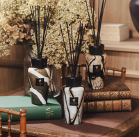 Three marble-patterned reed diffusers, including the elegant Baobab Stones Diffuser - Agate, sit atop stacked books, surrounded by wooden furniture and dried hydrangea flowers, creating a cozy and refined atmosphere that elevates any home fragrance experience.