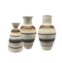 The Carina Vase - Small by Mood Dekor features a sculptural ceramic design with a wide body and narrow neck, adorned with horizontal brown, black, and beige stripes on a cream background. Displayed against a white backdrop, this piece is perfect for adding modern earthy decor to any space.
