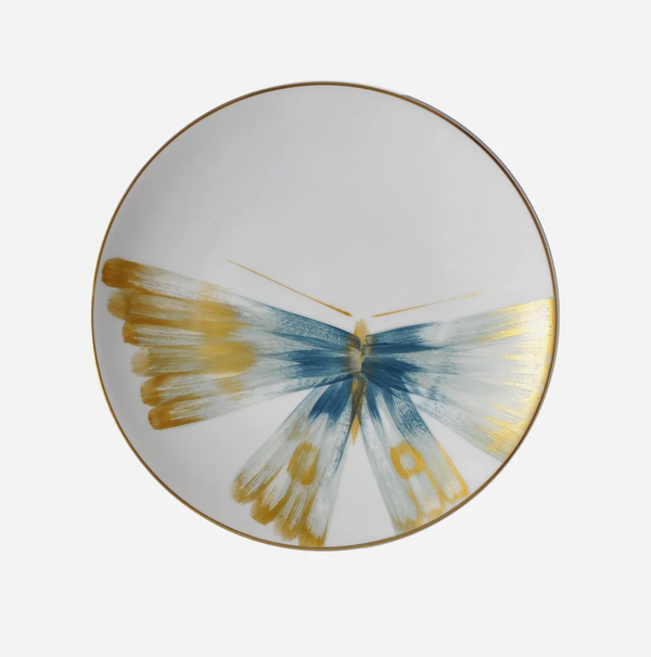 The Marie Daage Belle De Nuit 1 by Marie Daâge is a white plate with a gold rim, showcasing a hand-painted butterfly in shades of blue, gold, and white with its wings elegantly spread across the surface—an exquisite piece of tableware inspired by classic Limoges porcelain.