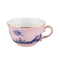 Light pink Oriente Italiano Dinnerware Azalea porcelain teacup featuring blue chinoiserie floral patterns and a gold-rimmed edge.