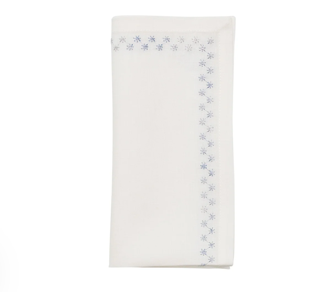 A folded Starry Night Napkin Set of 4 - White & Blue, featuring a blue metallic embroidery star pattern along the edge.